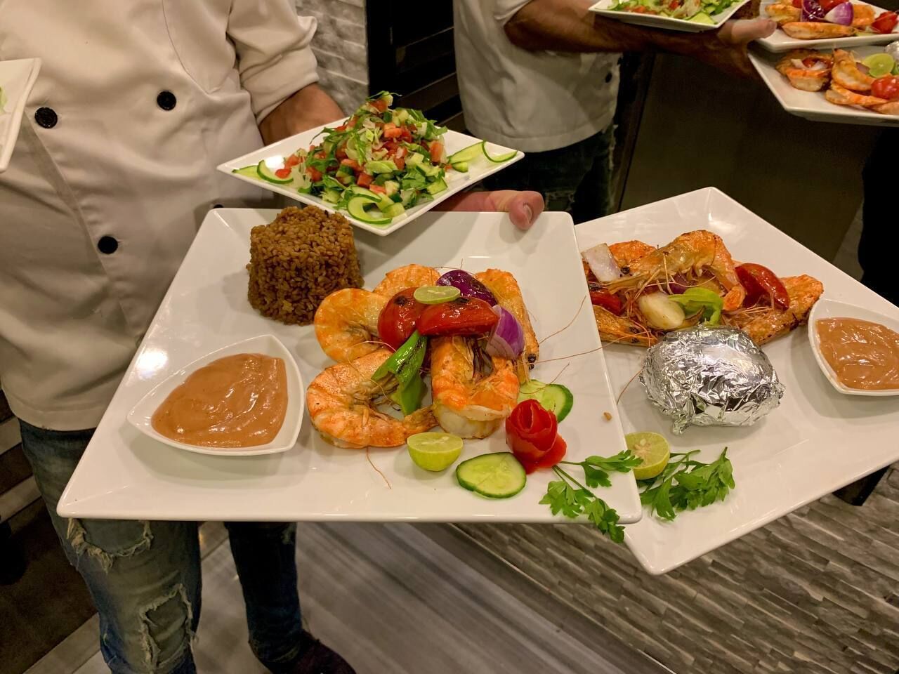 Una persona sosteniendo una bandeja con diversos platos, incluyendo camarones, ensalada y un alimento empanizado.