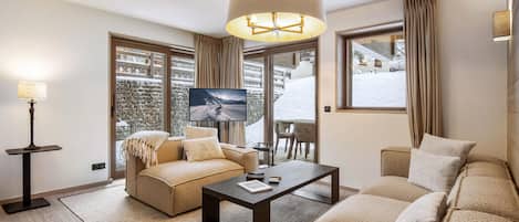 A modern living room with a sofa, a coffee table, and a TV. There is a large window with curtains, a floor lamp, and a view of a snowy landscape.