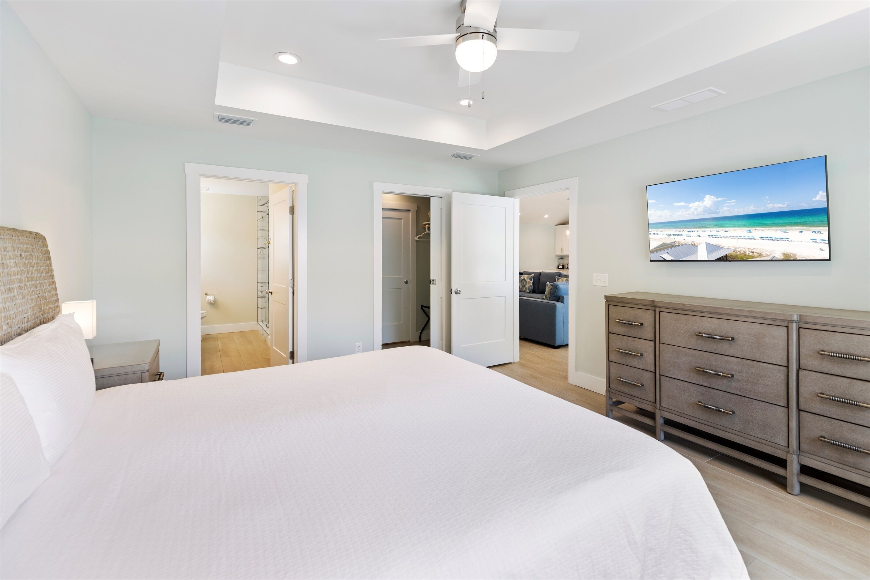 Un dormitorio con una cama grande, un ventilador de techo, un aparador y un televisor que muestra una escena de playa.