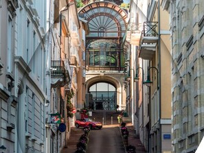 A narrow street with buildings on either side, a red car parked on the right, and a large arched entrance at the end. - Beautiful apartment with pets allowed in Évian (Évian-les-Bains)