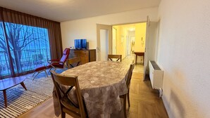 A dining area with a large table, chairs, and a television. There is a window with a view of trees and a door leading to another room. - Beautiful apartment with pets allowed in Évian (Évian-les-Bains)