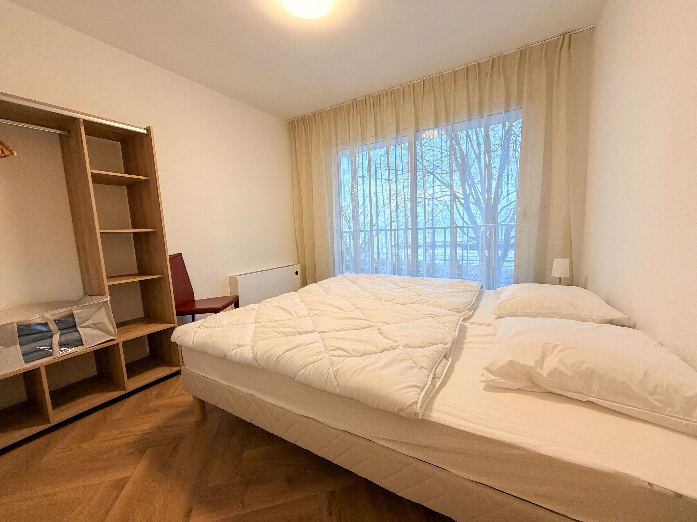 Een slaapkamer met een bed, een houten garderobe en een raam met gordijnen.