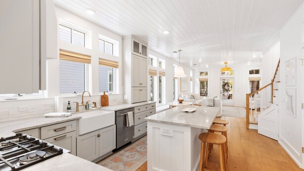 Een moderne keuken met witte kasten, een centraal eiland met krukken, en een houten vloer.
