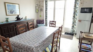 Ein Essbereich mit Tisch und Stühlen, ein Küchenbereich mit Kühlschrank und ein Fenster mit Vorhängen.