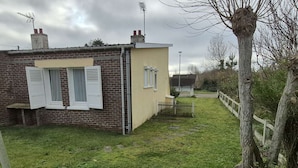 Ein kleines Backsteinhaus mit weißen Fensterläden, einem gelben Anstrich und einem gepflasterten Weg, der zu einem Tor führt.