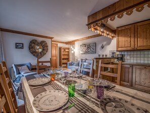 Zona pranzo con un lungo tavolo apparecchiato per un pasto, mobili contenitori in legno e un angolo salotto accogliente.