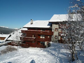 Un edificio a più piani con tetto imbiancato dalla neve, balconi in legno e facciata in pietra.