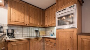 Une cuisine avec des meubles de rangement en bois, un four encastré, une machine à café et un dosseret carrelé.
