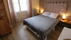 A bedroom with a bed, bedside lamps, a wooden nightstand, a radiator, and a window with curtains. - Cozy apartment in Luchon, 4 ppl, near spa, with parking (Bagnères-de-Luchon)