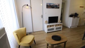A modern living room with a yellow armchair, a wooden coffee table, a flat-screen TV on a white cabinet, and a painting on the wall. - Cozy apartment in Luchon, 4 ppl, near spa, with parking (Bagnères-de-Luchon)