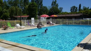 Una piscina con sillas de descanso y sombrillas, rodeada por una valla.