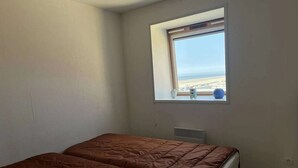A room with two beds, a window with a view of the beach, and a small table with a vase. - 3-Bedroom Apt near beach, with garage (Cucq-Stella Plage)