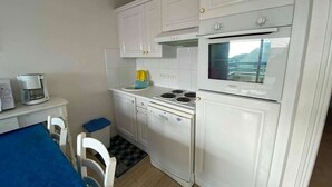 A compact kitchen with white cabinets, a stove, and a coffee maker. - 3-Bedroom Apt near beach, with garage (Cucq-Stella Plage)