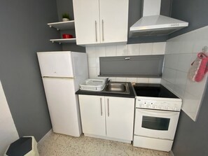 Eine kleine Küche mit weißen Schränken, einem eingebauten Backofen, einem Kochfeld und einem Spülbecken.