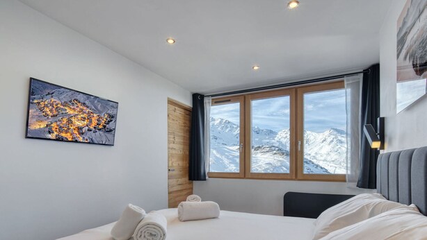Ein modernes Hotelzimmer mit einem großen Bett, einem Gemälde einer Vulkanlandschaft, einem Fenster mit Bergblick und einer Holztür.