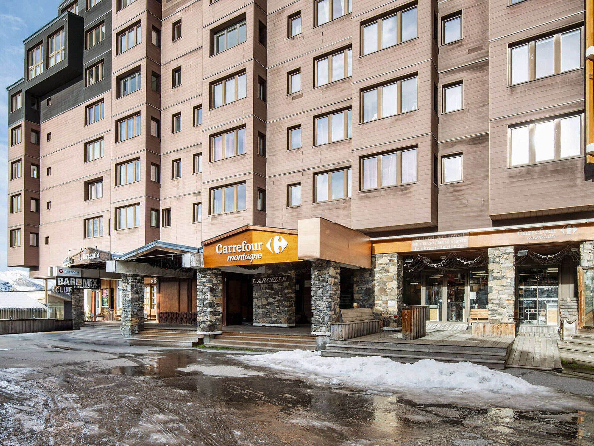 Ein mehrstöckiges Hotel mit steinverkleideter Fassade, ein Carrefour Montagne Geschäft und ein Bar & Mix Club.