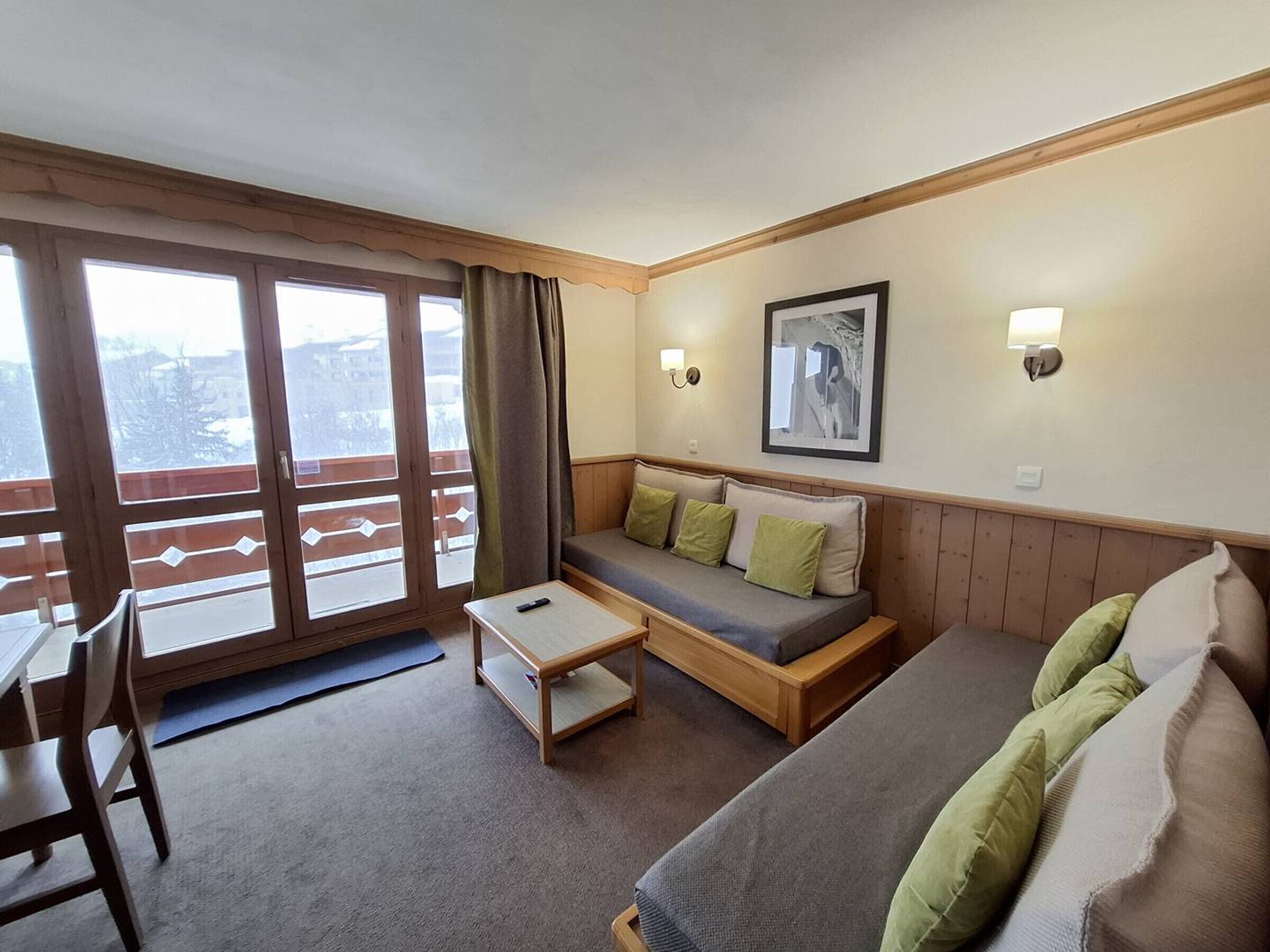 Une pièce confortable avec un canapé, une petite table, une chaise et un balcon doté de grandes fenêtres.