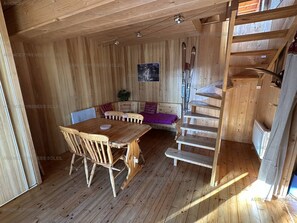 Ein Holzblockbau-Innenraum mit Esstisch, Stühlen, einer Bank und einer Treppe.