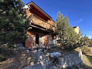 Eine Holzhütte mit Balkon, umgeben von Kiefern und einer Steismauer.