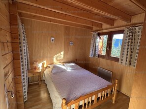 Ein Schlafzimmer einer Holzhütte mit Bett, Nachttisch, Fenster mit Vorhängen und Heizkörper.
