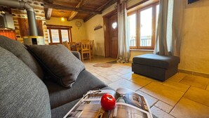 Un salon confortable avec un canapé, une table entourée de chaises, une cheminée et une fenêtre agrémentée de rideaux.