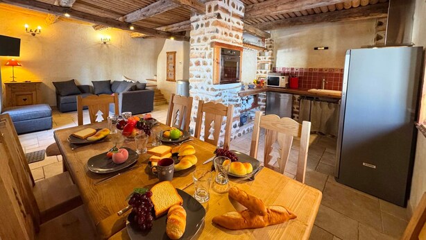 Une cuisine rustique aux murs de pierre, aux poutres apparentes et dotée d’un coin repas avec une table mise pour le repas.