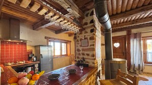 Une cuisine rustique avec un mur en pierre, des poutres en bois, un meuble à vin intégré et une table en bois accompagnée d’une chaise.
