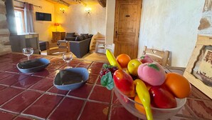 Une pièce rustique avec un plafond en bois, un canapé, une table à manger agrémentée d’un panier de fruits et une porte en bois.