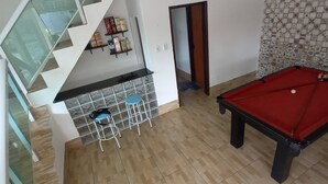 Ett rum med ett biljardbord, en bardisk med barstolar och en trappa med glasräcken.