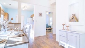 Una cocina amplia con piso de madera, muebles blancos y un comedor con mesa para cuatro.