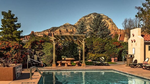 Zona de piscina con pérgola, sillas de descanso y montañas al fondo.