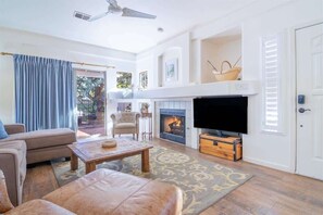 Ein Wohnzimmer mit Sofa, Couchtisch, Fernseher, Kamin und einer Tür.