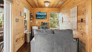 Ein Interieur einer Holzblockhütte mit einer Couch, einem Gemälde, einer Mikrowelle und Blick auf einen See.