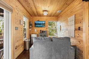 A log cabin interior with a sofa, a painting, a microwave, and a view of a lake. - Upper & Lower Oasis - Team Joseph Ellen (St. Augustine)