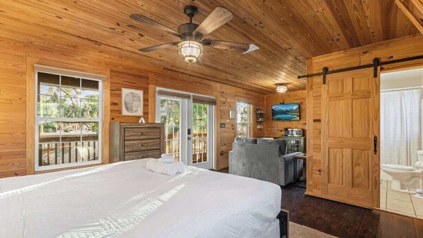 Ein Schlafzimmer einer Holzhütte mit Bett, Deckenventilator, Fernseher und einer Schiebetür.