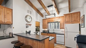 A kitchen with wooden cabinets, a central island with stools, a clock, and a refrigerator. - 3BR/2.5BA Incline Village condo, pool, fireplace (Incline Village)
