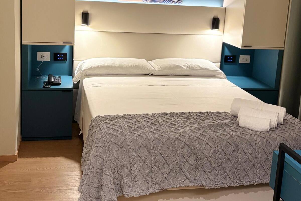 A modern hotel room with a bed, bedside tables, a wall-mounted artwork, and a blue accent wall.