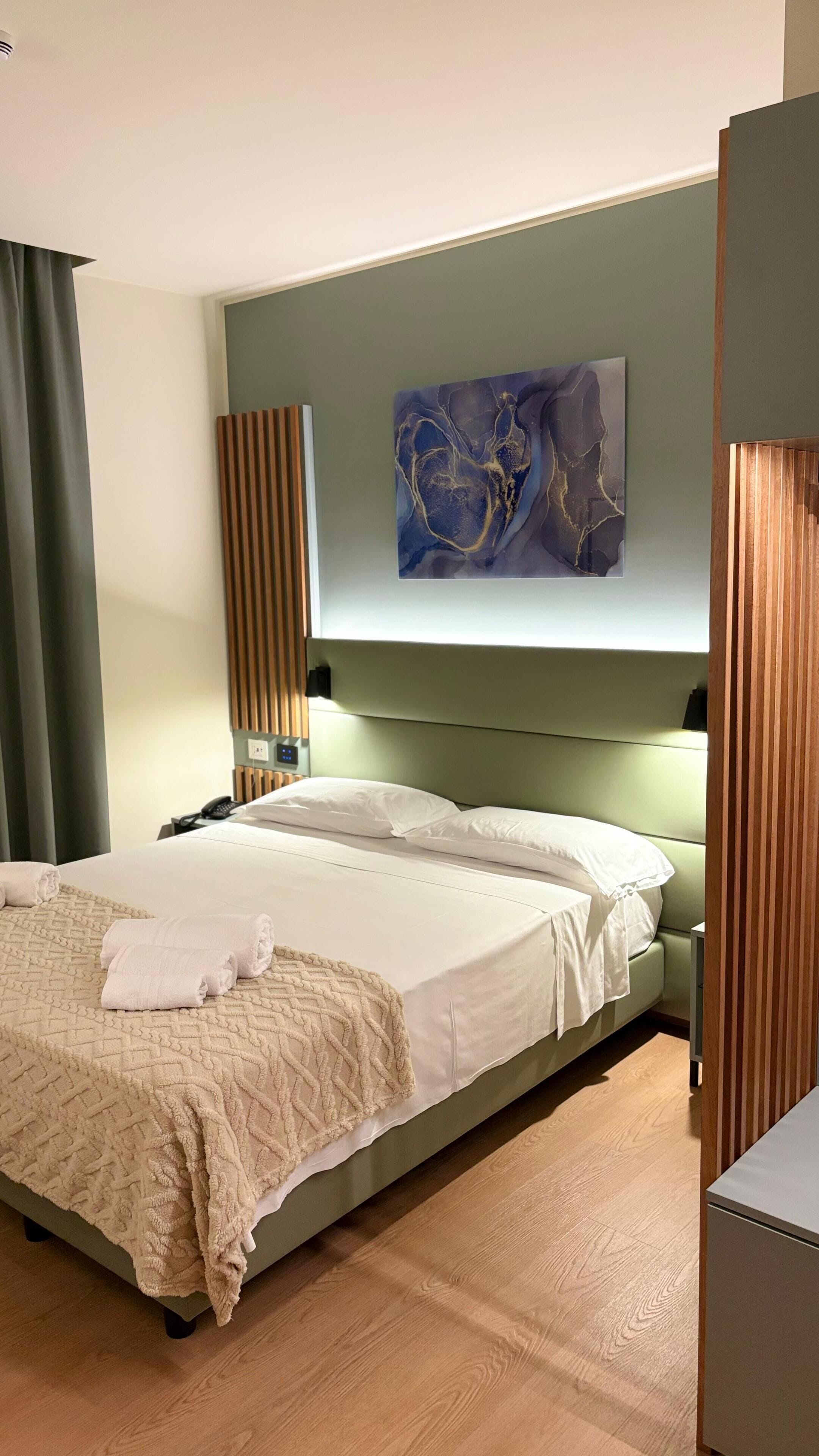 A hotel room with a bed, a bedside table, a lamp, and a painting on the wall.
