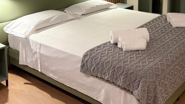 A modern hotel room with a large bed, a headboard with a built-in TV, a bedside table with a lamp, and a wall-mounted artwork. - Hotel Milazzo Smart (Milazzo)