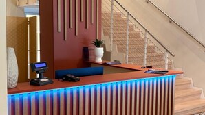 A modern reception desk with a built-in digital display, a potted plant, and a staircase in the background. - Hotel Milazzo Smart (Milazzo)