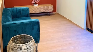 A modern living room with a teal sofa, a flat-screen TV mounted on a red wall, a wooden console table with a potted plant, and a wicker basket. - Hotel Milazzo Smart (Milazzo)