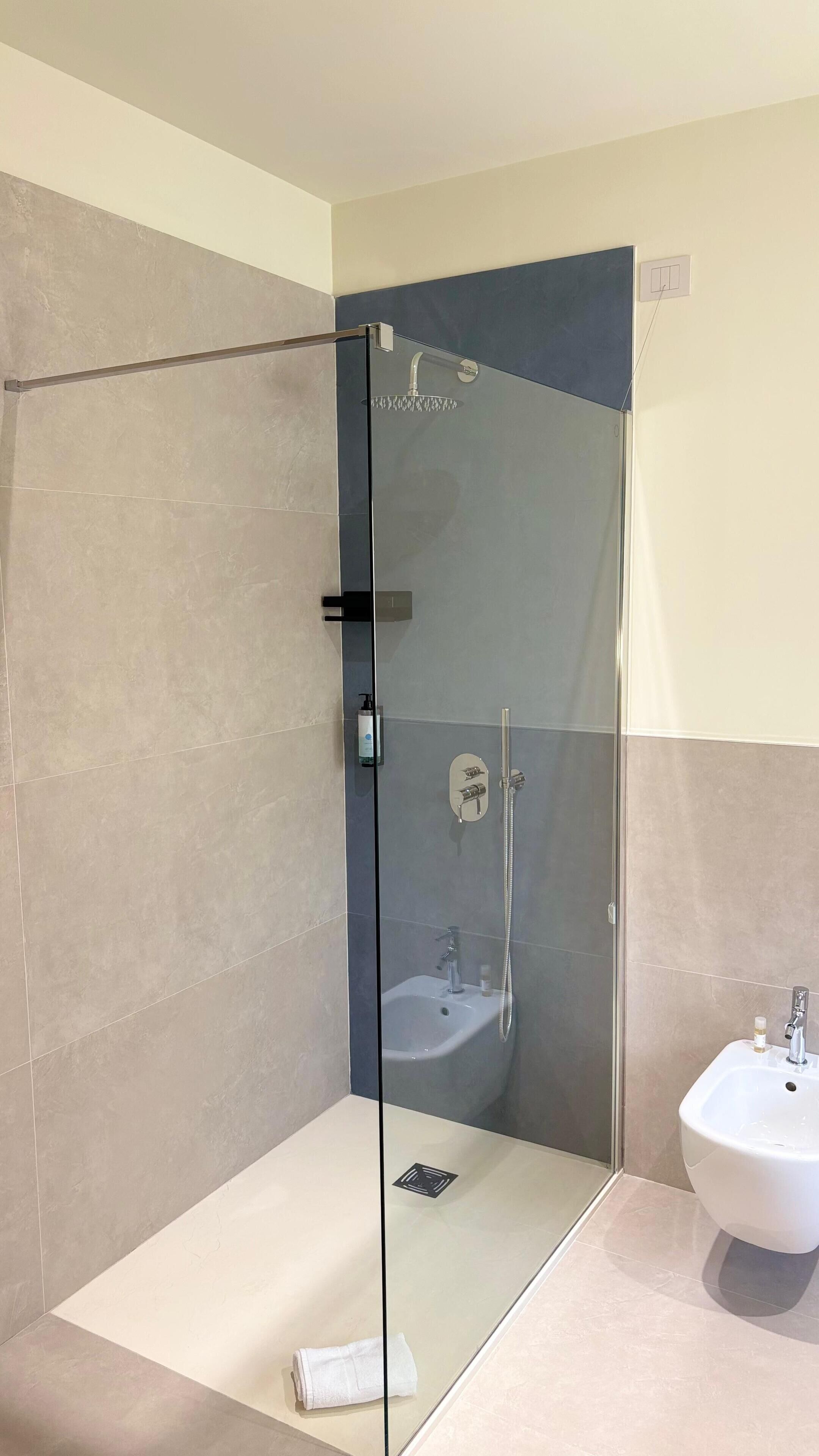 A modern bathroom with a glass-enclosed shower, a white sink, and a towel on the floor.