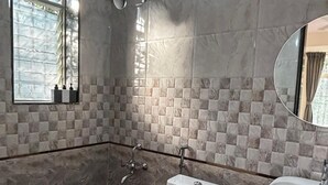 Un baño con inodoro, bidé y lavamanos, paredes con azulejos y una ventana con persianas.
