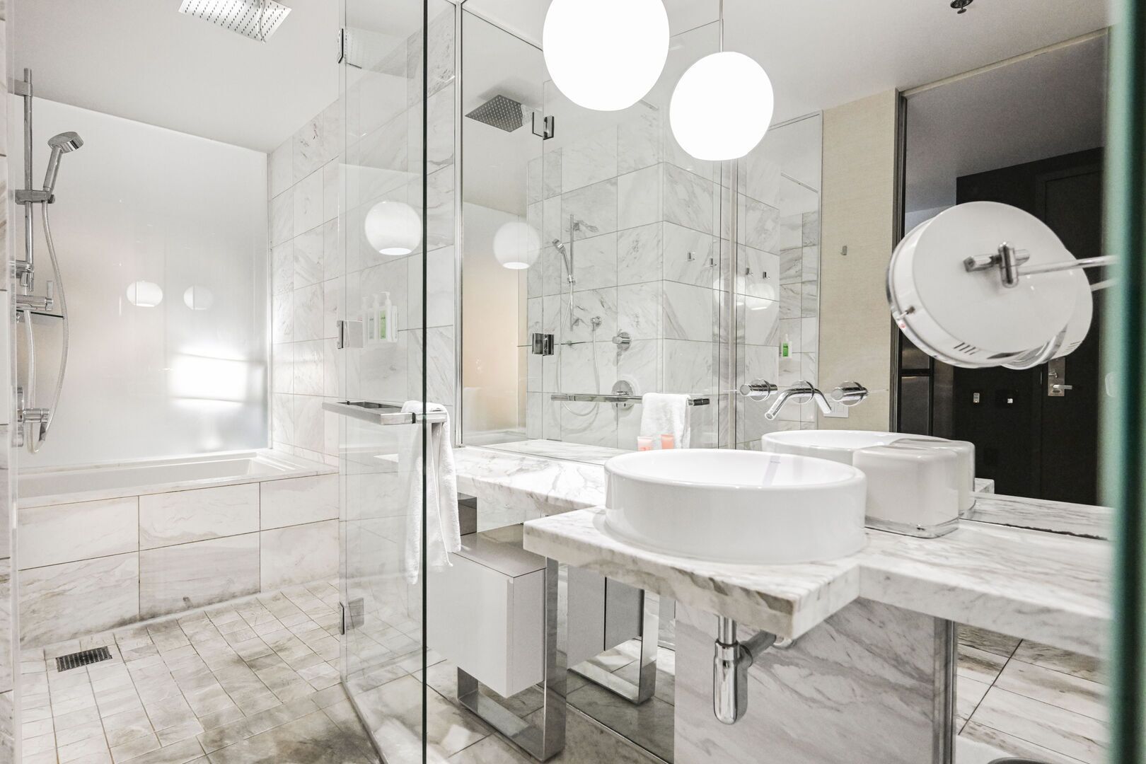 Une salle de bain moderne dotée d’une douche à parois de verre, de deux lavabos et d’un grand miroir.