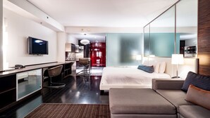 Een moderne hotelkamer met een bed, bureau, stoel, televisie en een grote spiegel.