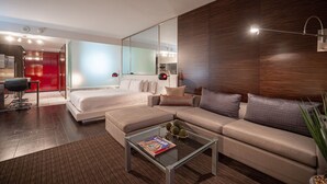 Une chambre d’hôtel moderne avec un grand lit, un canapé, une table basse en verre et un grand miroir.