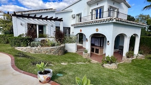 A two-story house with a white exterior, a balcony with a black railing, and a stone foundation. - 18 - Villa 1km from the beach in Calahonda/Mijas (Mijas Costa)