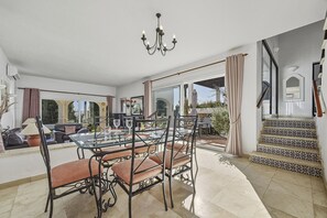Ein großzügiger Essbereich mit Glastisch, Metallstühlen, einer Deckenleuchte und Blick auf die Terrasse.