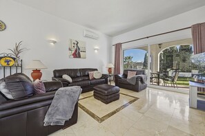 Ein modernes Wohnzimmer mit einer Couch, einem Hocker und einem Essbereich mit Tisch und Stühlen.
