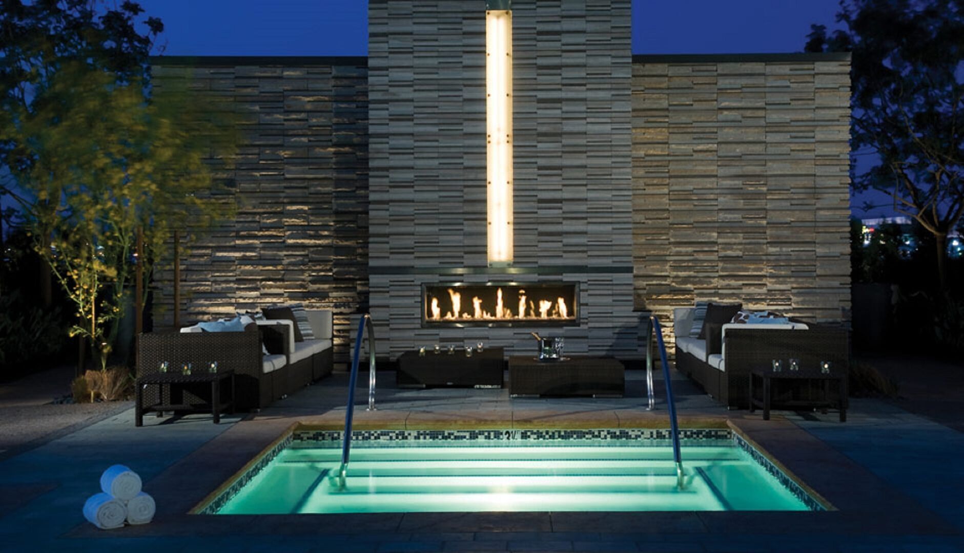 A modern outdoor pool area with a stone wall and a built-in fireplace.